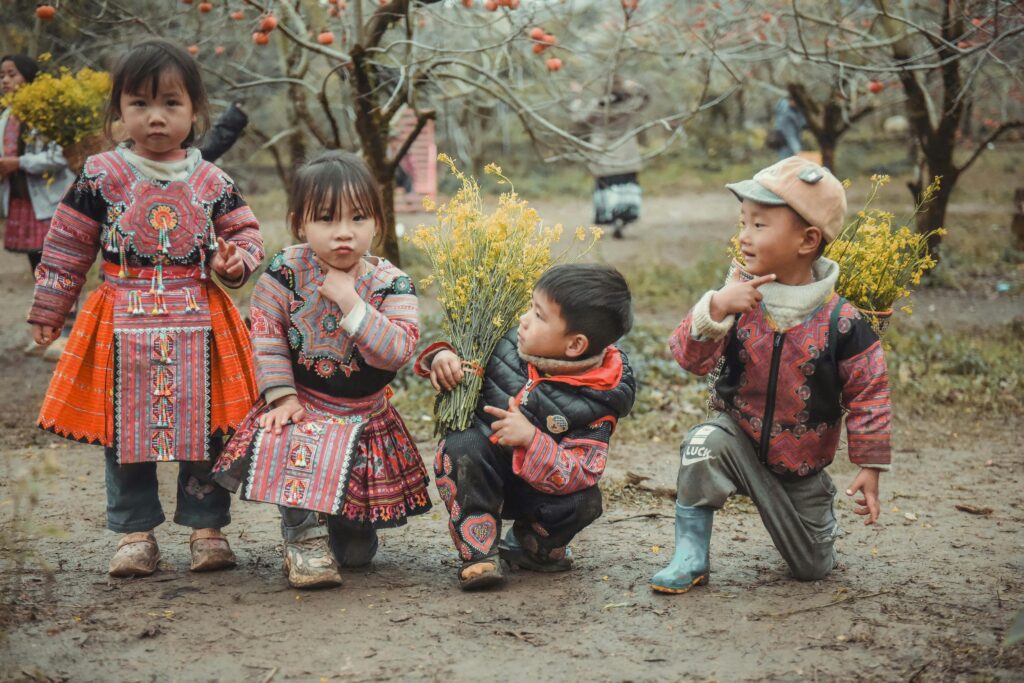 Group of children in vibrant traditional dress playing in an orchard holding flowers.